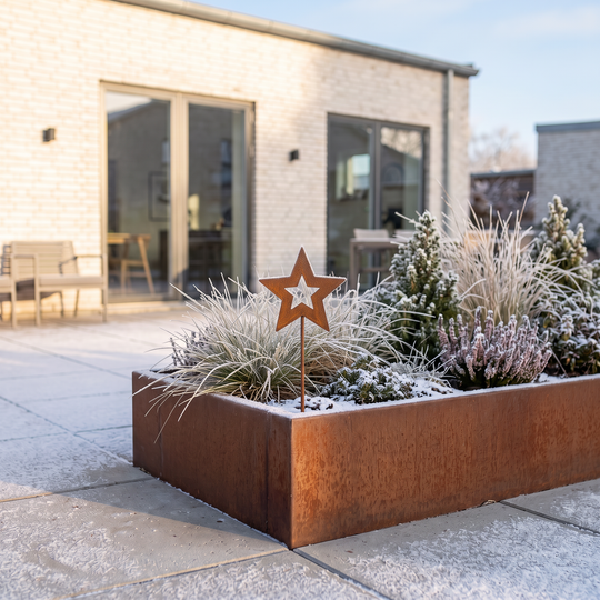 Hochbeet aus Cortenstahl mit Gartenstecker in Sternform auf einer frostigen Terrasse vor einem hellen Backsteinhaus.