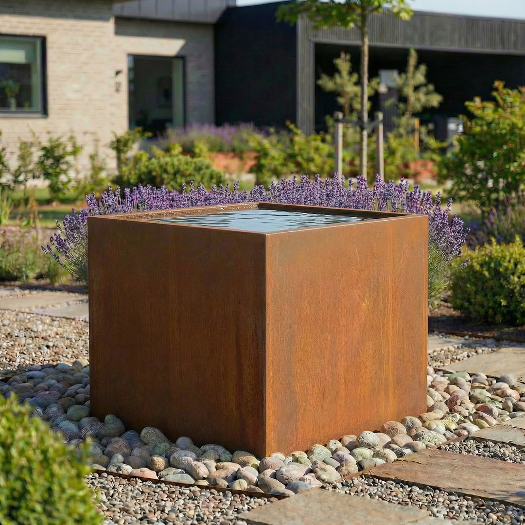 Eine höher Wasserbecken aus cortenstahl in einem schönen garten.  